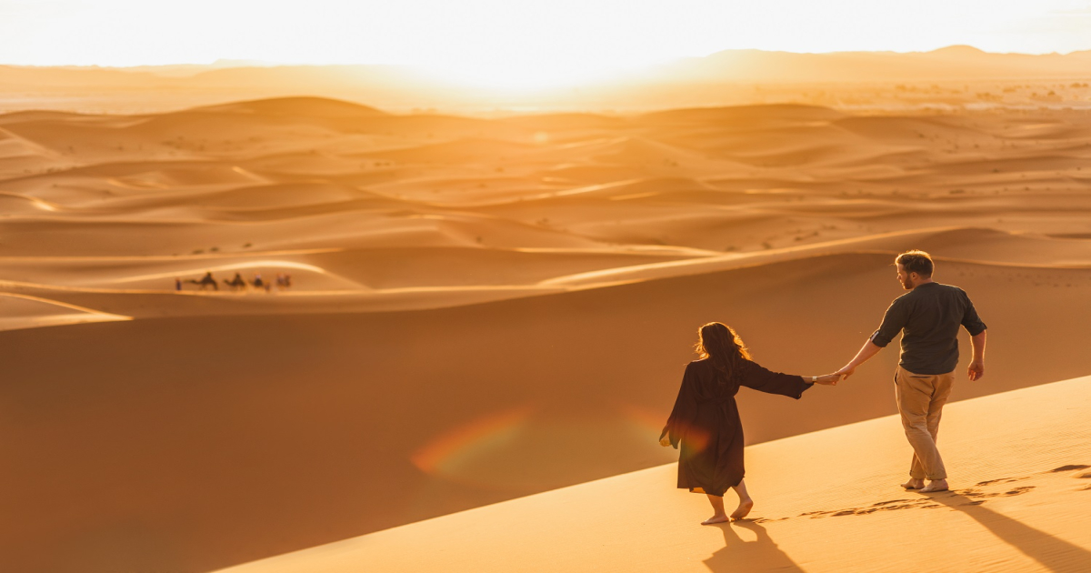 Una pareja cogida de la mano en el desierto de Merzouga feliz tras ahorrarse el viaje en Marruecos