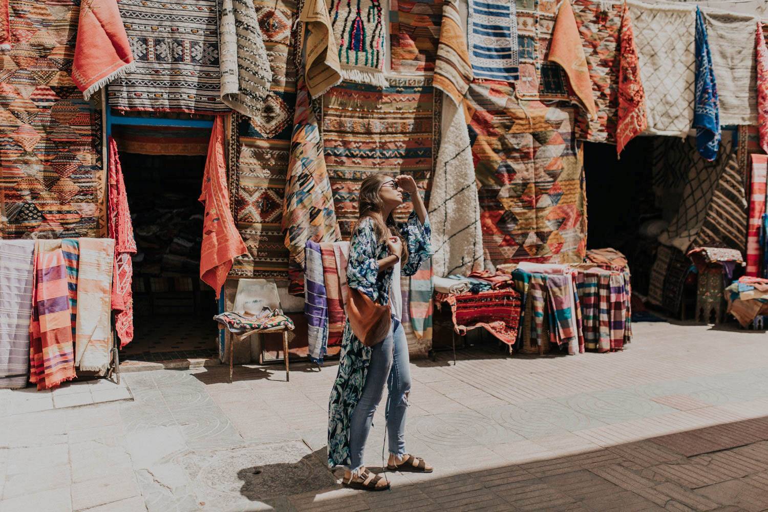 Mujer viajando sola explorando un zoco marroquí con coloridas alfombras en exhibición