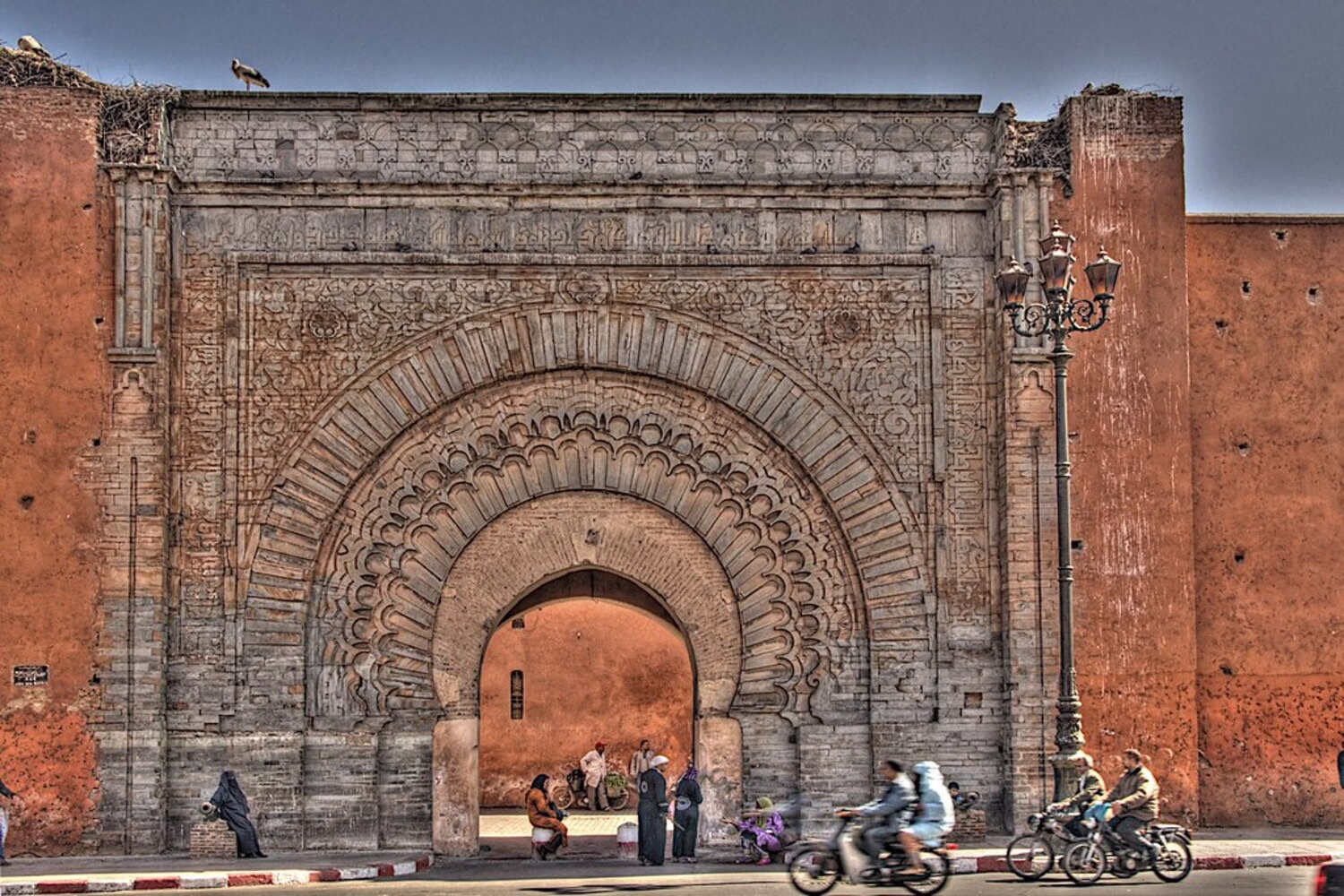 Puerta de la ciudad Bab Agnaou en las antiguas murallas de Marrakech, uno de los lugares históricos de Marruecos, con lugareños y motocicletas pasando por delante