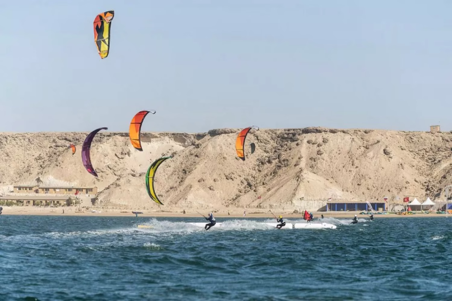 Kitesurfistas en la laguna de Dajla, Marruecos, con acantilados desérticos de arena al fondo.