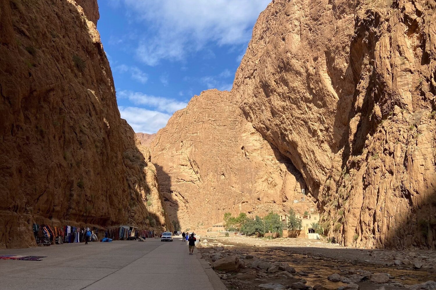 Gargantas del Todra, Marruecos: viajeros caminando entre las altas paredes anaranjadas del cañón y el río poco profundo cerca de Tinghir.