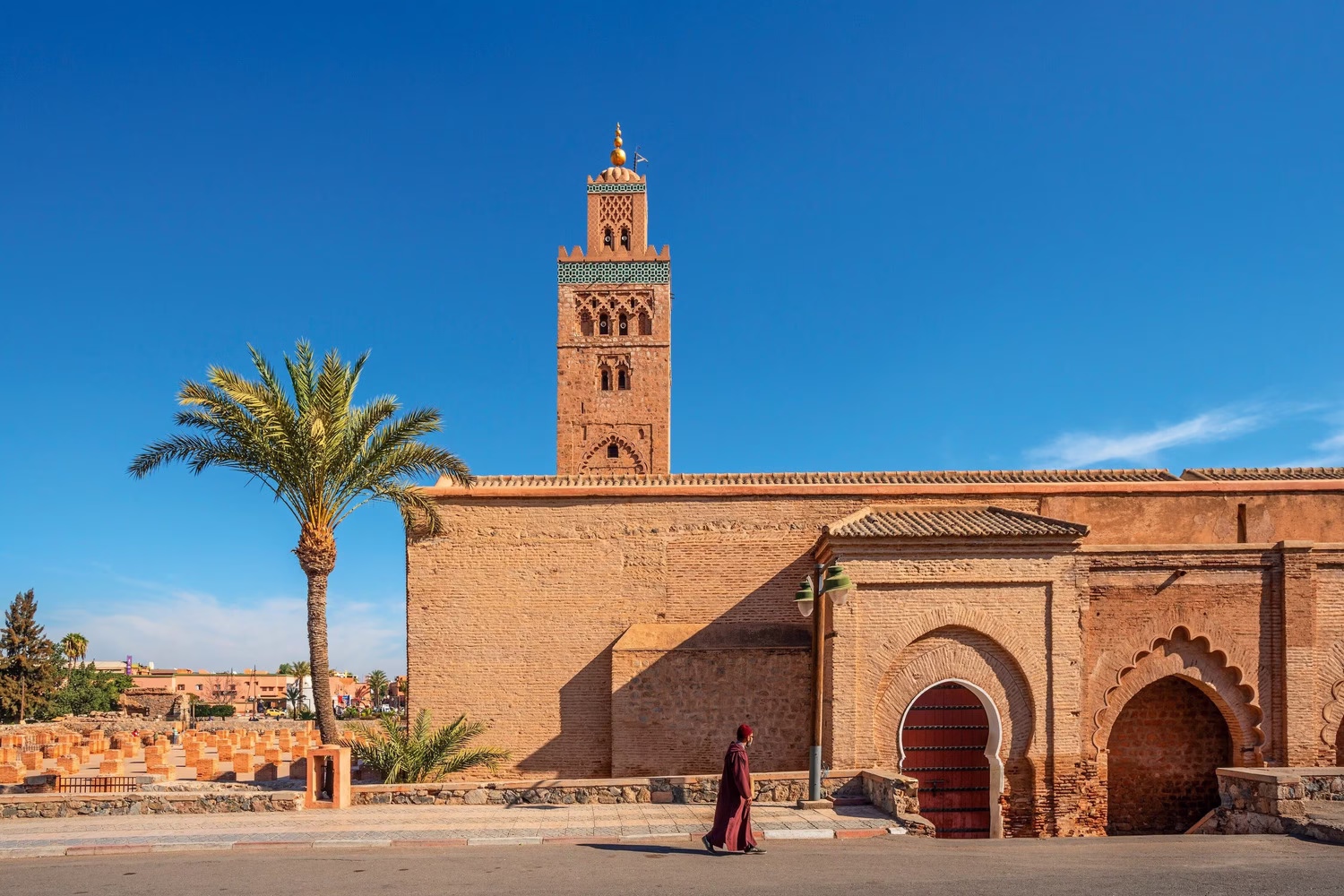 Hombre caminando junto a la Mezquita Kutubía en Marrakech, ilustrando la vestimenta y el comportamiento respetuosos para los viajeros que aprenden qué hacer y qué no hacer en Marruecos.