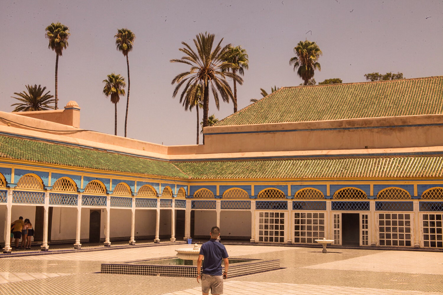 Patio del Palacio de la Bahía en Marrakech con arcos tradicionales marroquíes, tejados de tejas verdes, palmeras y una fuente central