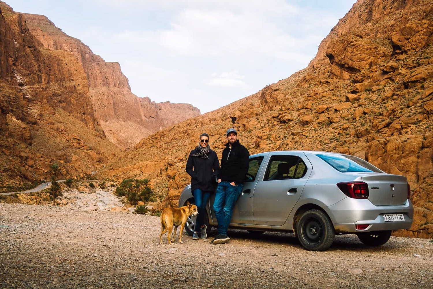 Alquilar un coche en Marruecos con viajeros parando en un pintoresco cañón de montaña, mostrando la libertad de un viaje por carretera y el turismo fuera de las rutas habituales en Marruecos