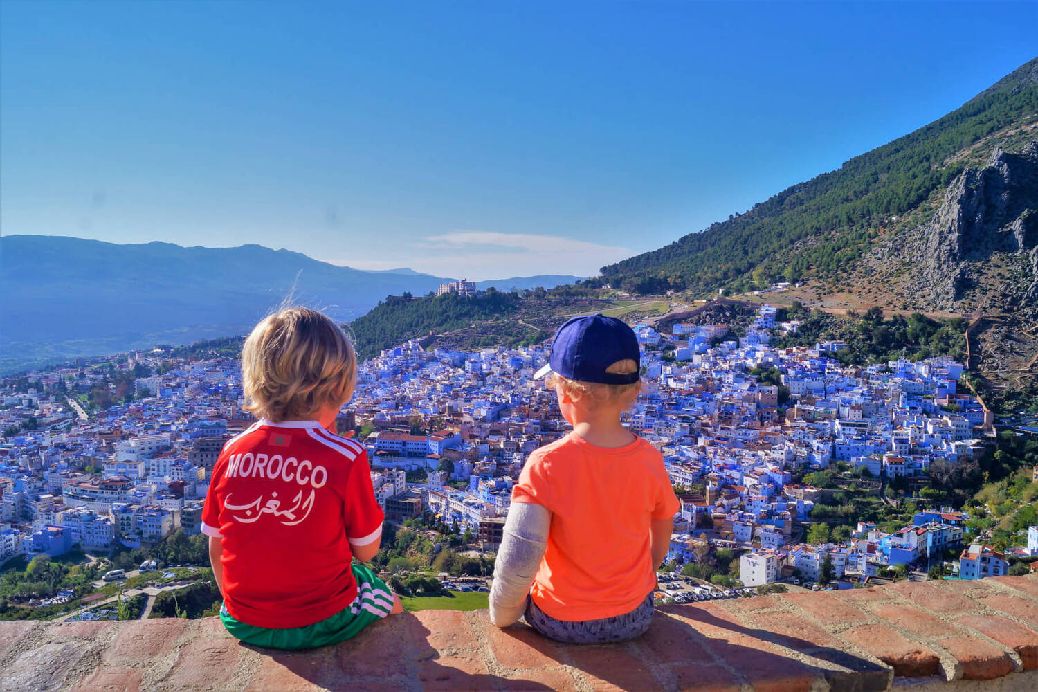 Dos niños mirando la ciudad azul de Chefchaouen, Marruecos, desde un mirador con montañas al fondo
